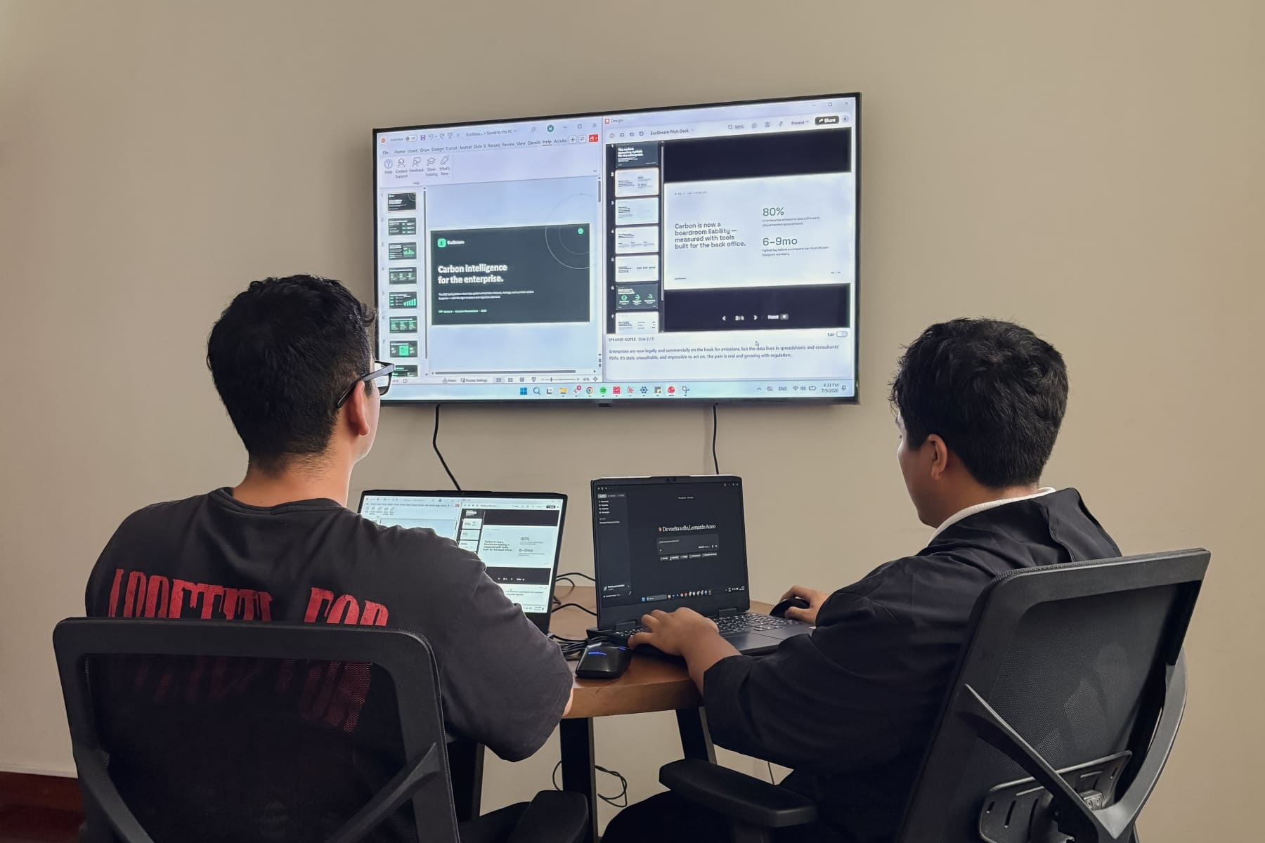 24Slides team members Adimir Sanchez (left) and Leo (right) collaborating in front of a monitor to manually fix a Claude AI-generated presentation in PowerPoint.