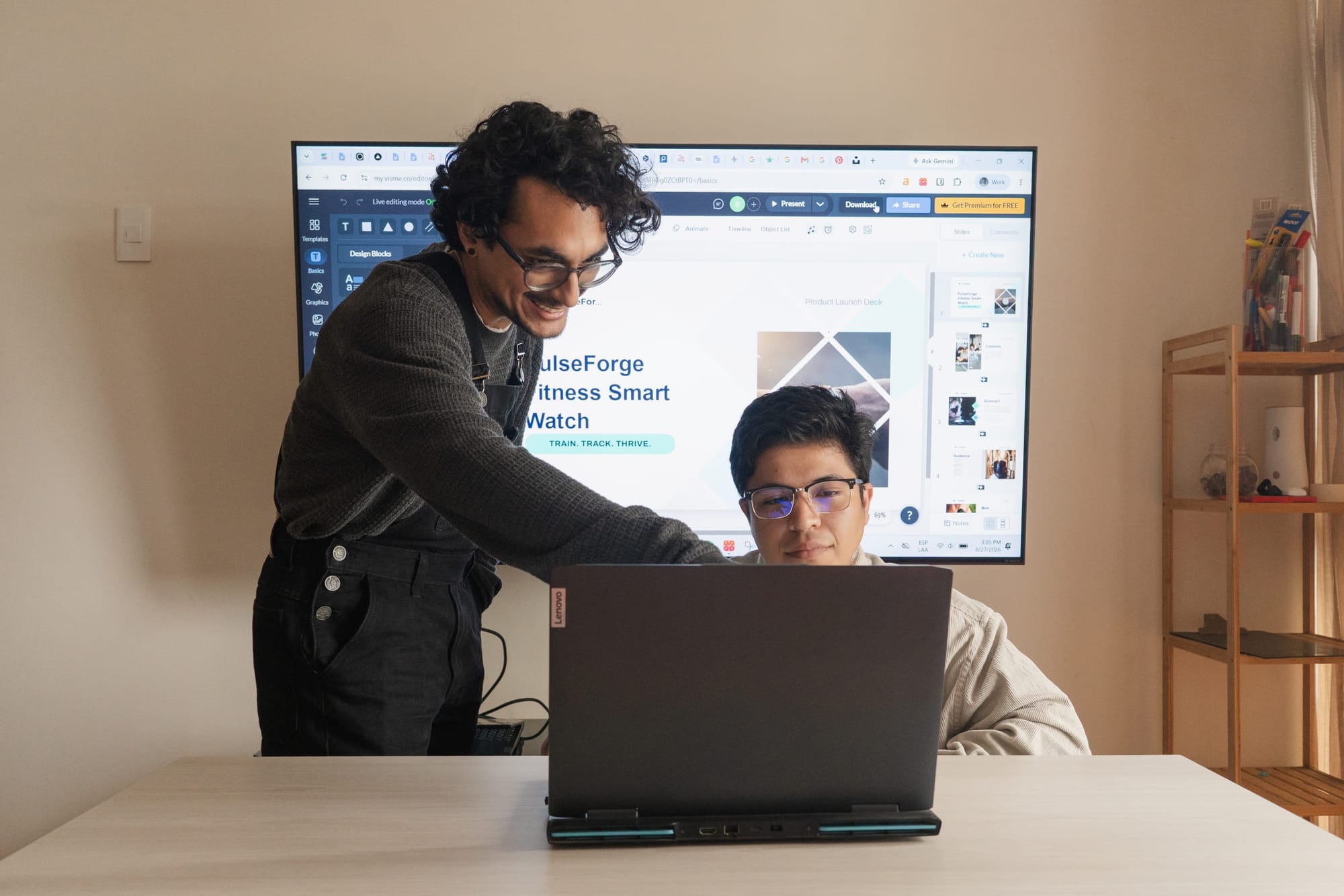 24Slides presentation designers Gabriel Morales (left) and Leonardo Acaro (right) collaborating on a laptop while stress-testing the Visme platform, with the software interface visible on a large monitor behind them.