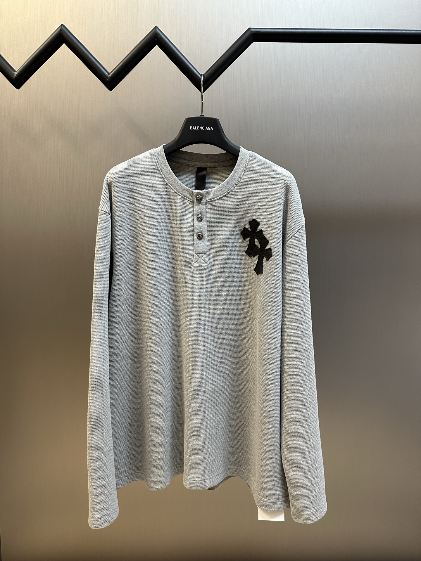 Chrome Hearts Chrome Hearts Cross Silver Button Long Sleeve Customized pure cotton waffle fabric, decorated with a Croix heart cross leather on the chest, the tough edges of the leather pierce the softness of the gray. The hand-stitched logo buckle is like a miniature work of art, and the logo plate on the back sways slightly with the swing of the body, adding a sense of movement and vitality.