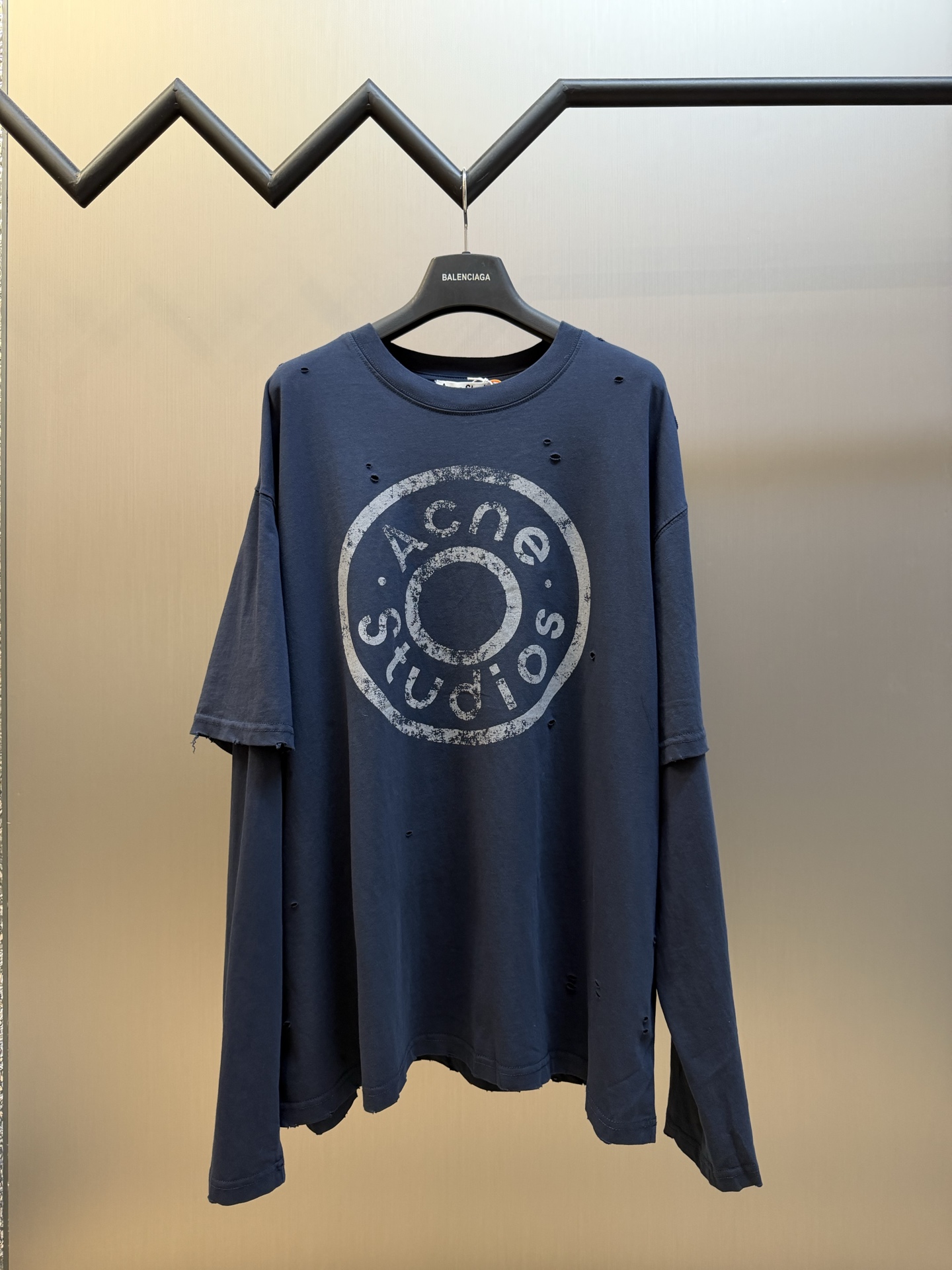 Ac Studios Distressed Logo Fake Two Piece Long Sleeve Customized plain cotton with weft sequence, neat round neck, simple and restrained, layered structure cleverly creates fake two-piece layers, short sleeves stacked on long sleeves for a three-dimensional look, the chest is embellished with the seasonal denim-style rivet logo, retro marks are dimly deposited on the fabric, the body is staggered with frayed holes, and the natural texture of the fabric is deconstructed, and the loose shoulder silhouette is relaxed.