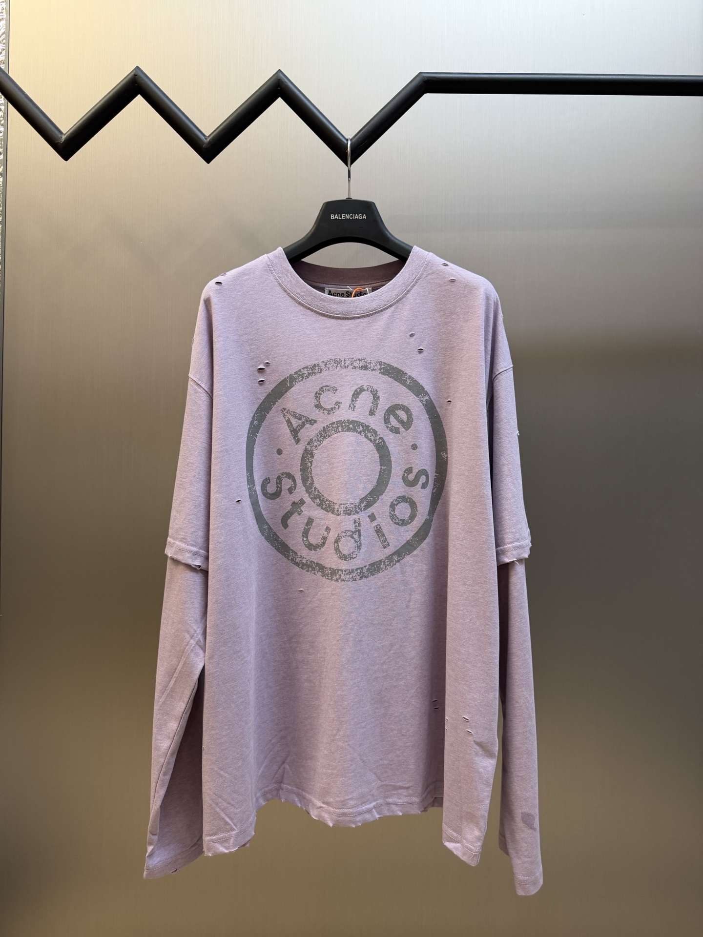 Ac Studios Distressed Logo Fake Two Piece Long Sleeve Customized plain cotton with weft sequence, neat round neck, simple and restrained, layered structure cleverly creates fake two-piece layers, short sleeves stacked on long sleeves for a three-dimensional look, the chest is embellished with the seasonal denim-style rivet logo, retro marks are dimly deposited on the fabric, the body is staggered with frayed holes, and the natural texture of the fabric is deconstructed, and the loose shoulder silhouette is relaxed.