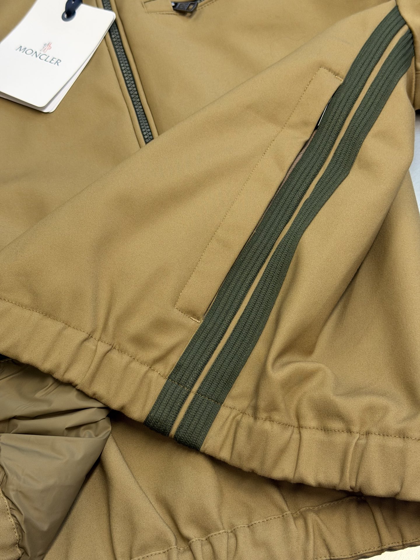 Moc logo pocket zip jacket Customized Mo Chen Yujing cotton brocade blend, three-dimensional stand-up collar creates a smart aura, the main zipper and chest pocket zipper use contrasting teeth, showing exquisite craftsmanship in details. Double green webbing runs vertically through the side of the body, injecting retro sports lines, round logos on the sleeves and arms are implicitly embellished, and elastic cuffs stabilize the version. It combines urban functionality and retro sports aesthetics, interpreting Italian quiet luxury style. - Image 7