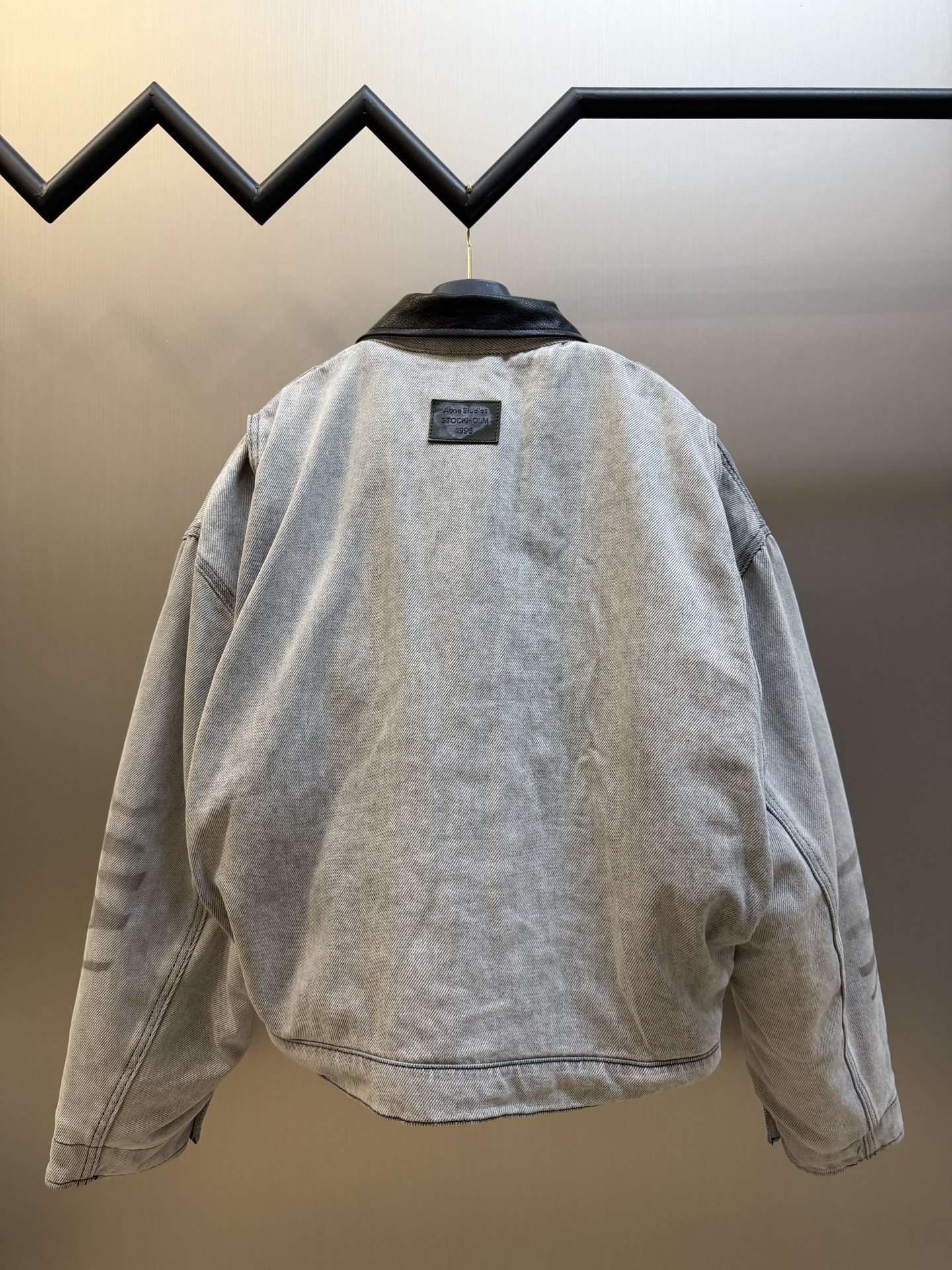 Ac Studios distressed leather cotton denim jacket The outer layer is custom-made weft-ordered organic denim, and the inner layer is custom-made domain-ordered plaid cotton. The entire body is covered in a matte gray tone. The original faded texture is naturally generated. The black leather collar is neatly cut and spliced. The roughness of the denim blends with the smoothness of the leather, creating a collision of rich layers of materials. The arms are embossed with dark patterns, and the patterns are dimly visible. The classic leather label on the back of the neck is properly seated, and the brand's collection imprint is hidden on the back. - Image 4
