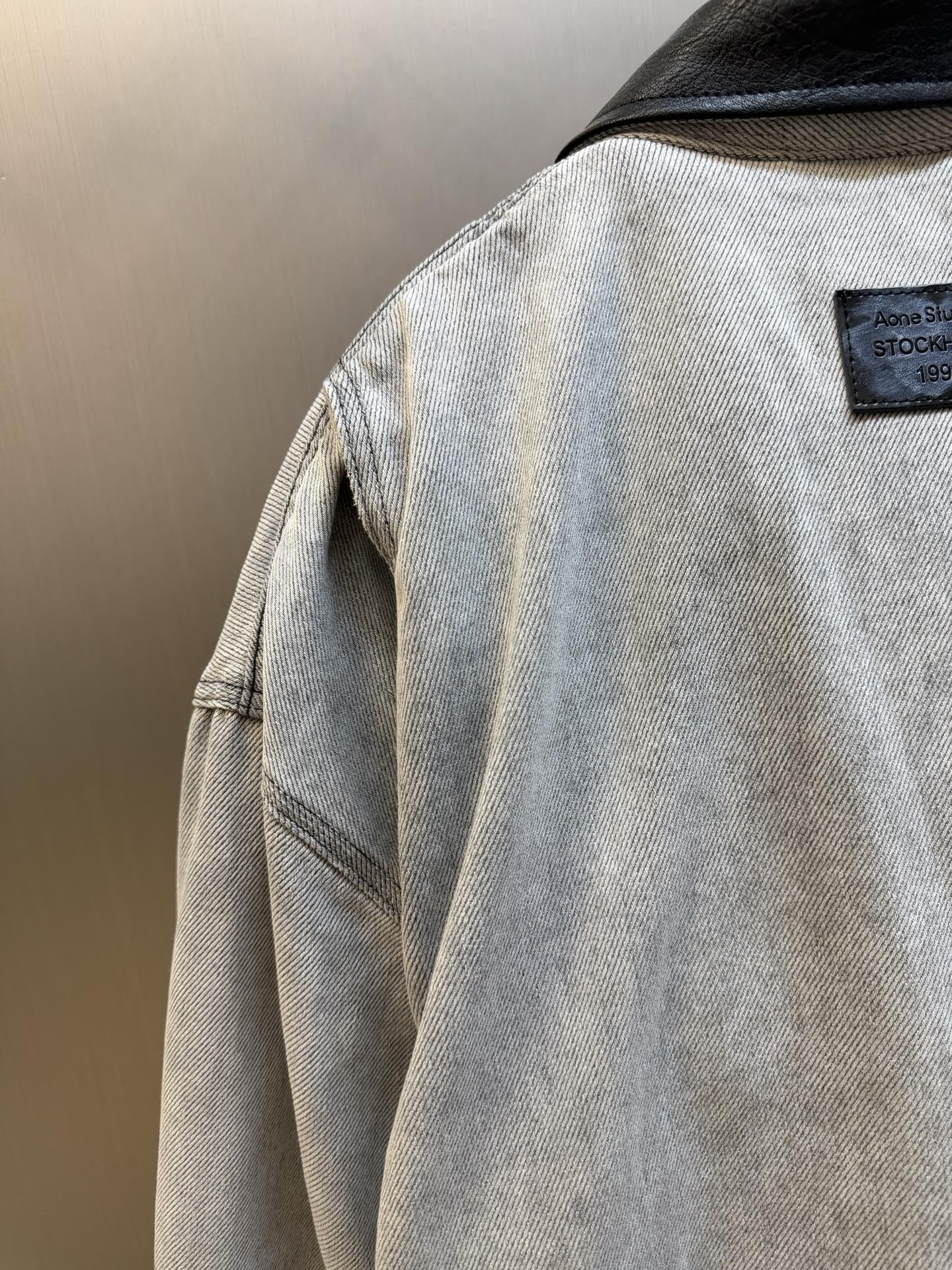Ac Studios distressed leather cotton denim jacket The outer layer is custom-made weft-ordered organic denim, and the inner layer is custom-made domain-ordered plaid cotton. The entire body is covered in a matte gray tone. The original faded texture is naturally generated. The black leather collar is neatly cut and spliced. The roughness of the denim blends with the smoothness of the leather, creating a collision of rich layers of materials. The arms are embossed with dark patterns, and the patterns are dimly visible. The classic leather label on the back of the neck is properly seated, and the brand's collection imprint is hidden on the back. - Image 5