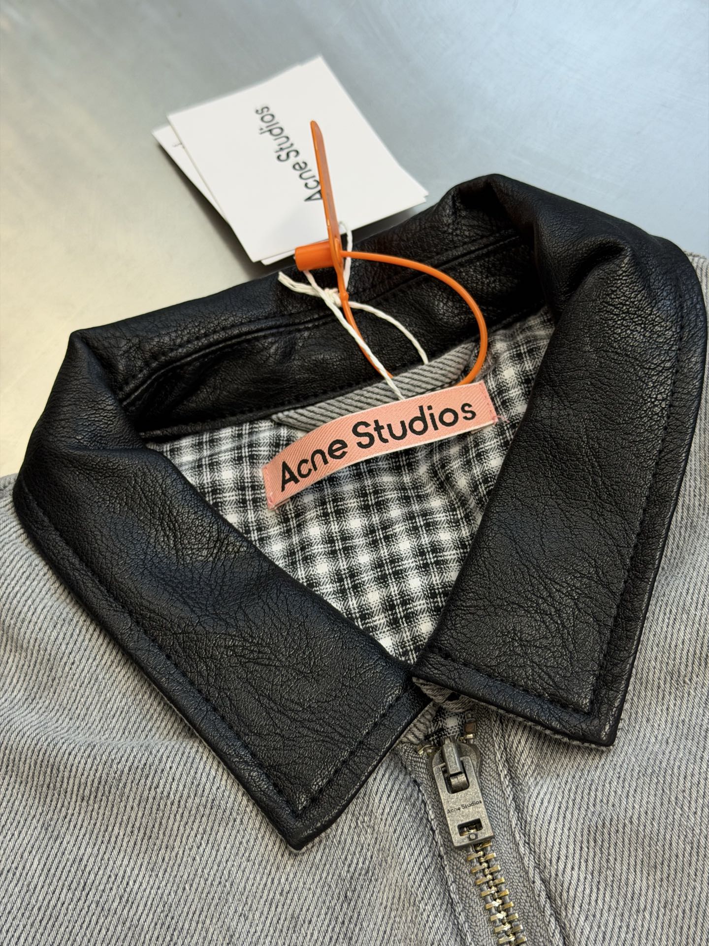 Ac Studios distressed leather cotton denim jacket The outer layer is custom-made weft-ordered organic denim, and the inner layer is custom-made domain-ordered plaid cotton. The entire body is covered in a matte gray tone. The original faded texture is naturally generated. The black leather collar is neatly cut and spliced. The roughness of the denim blends with the smoothness of the leather, creating a collision of rich layers of materials. The arms are embossed with dark patterns, and the patterns are dimly visible. The classic leather label on the back of the neck is properly seated, and the brand's collection imprint is hidden on the back. - Image 6