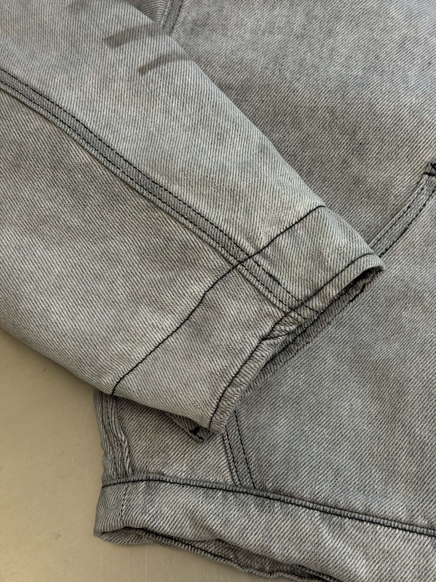 Ac Studios distressed leather cotton denim jacket The outer layer is custom-made weft-ordered organic denim, and the inner layer is custom-made domain-ordered plaid cotton. The entire body is covered in a matte gray tone. The original faded texture is naturally generated. The black leather collar is neatly cut and spliced. The roughness of the denim blends with the smoothness of the leather, creating a collision of rich layers of materials. The arms are embossed with dark patterns, and the patterns are dimly visible. The classic leather label on the back of the neck is properly seated, and the brand's collection imprint is hidden on the back. - Image 8