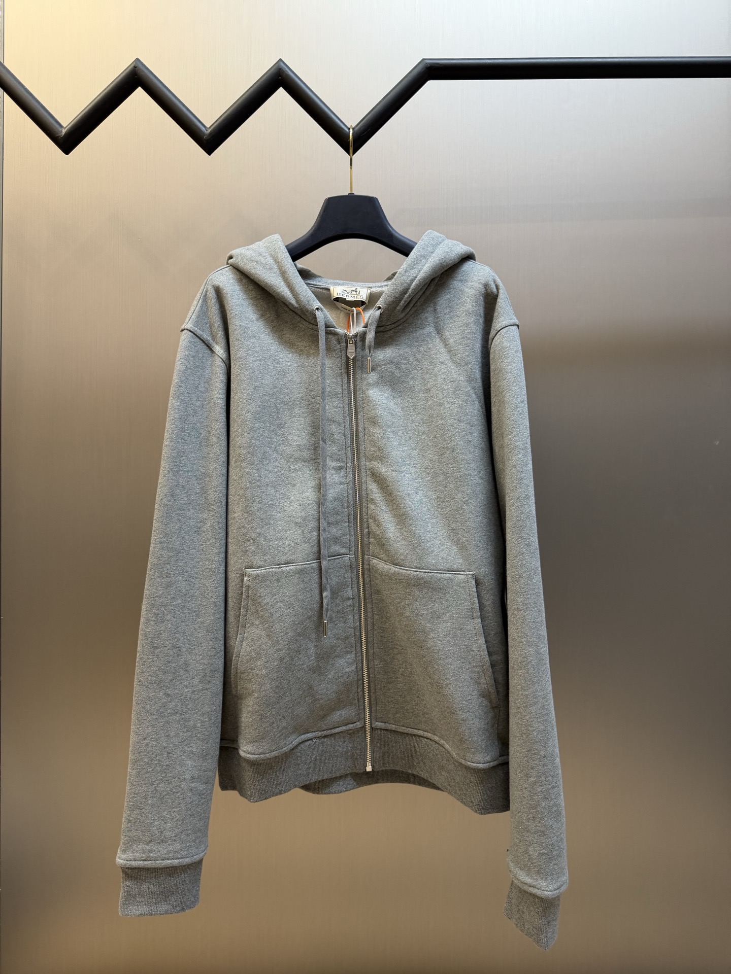 Hermès appliqué zippered jacket Customized wadding and heavy cotton velvet, a neat full-open zipper creates a smooth hooded configuration, the drawstring of the same color can be adjusted to the shape of the hood, and the kangaroo pocket hides practical ingenuity. The back is embellished with deconstructed equestrian totem patch printing, and the classic carriage and spur patterns are reconstructed through perspective art, laying out the brand's century-old equestrian heritage in the calm texture.