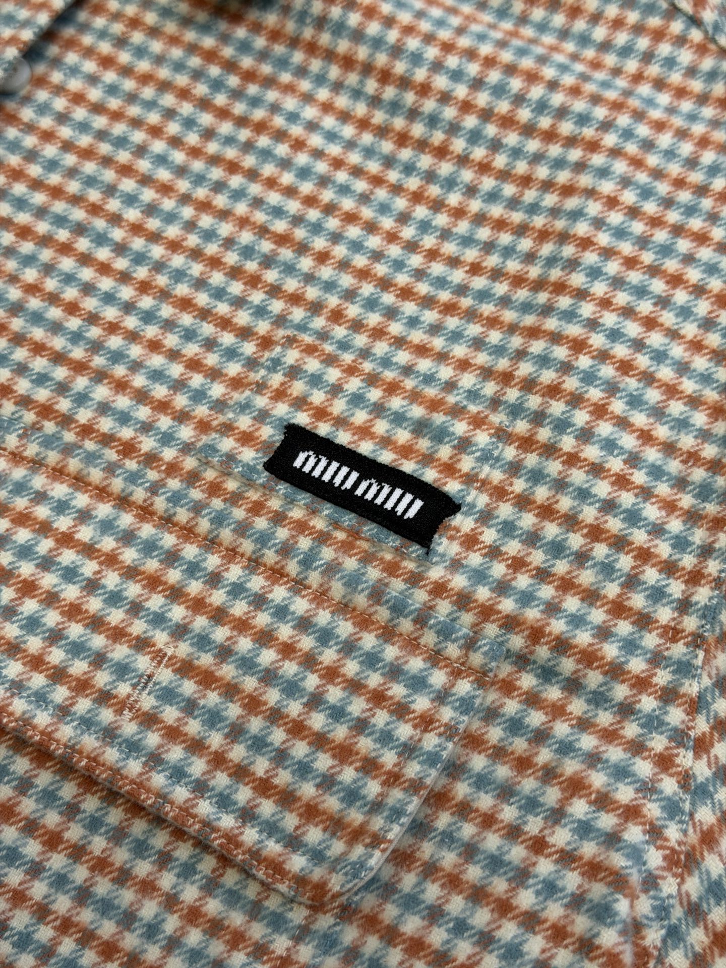 Miu logo checked shirt jacket Customized amber wool blend, woven with orange ocher and mint green warp and weft, fine yarn-dyed small plaid spreads over the body, matte fabric surface exuding Italian college retro charm, double patch pockets on the chest draping, integrating style layering and storage practicality, black embellished on the patch pockets The woven label logo is hidden in the staggered plaid texture, engraving the brand's family genes in every square inch - Image 6