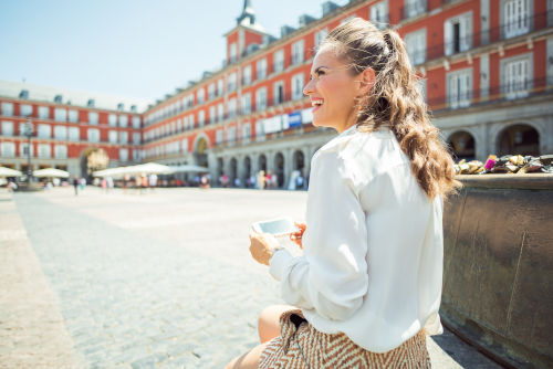 A tourist sitting in Madrid's Plaza Mayor with its red buildings and several arcades.