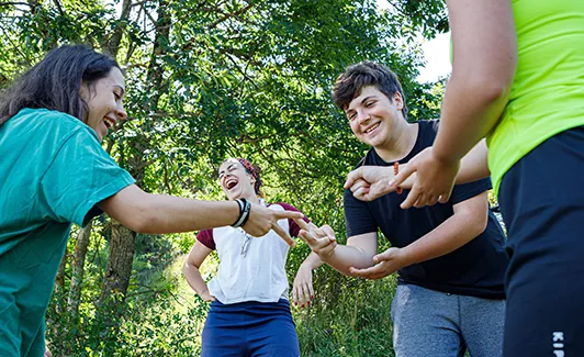 Grup de nens d' Escoltes Catalans jugant a pedra-paper-tisora mentre riuen, a un entorn boscós.