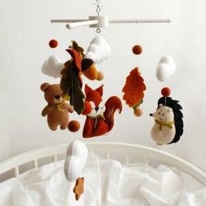 Hanging over the baby cot autumn forest woodland nursery crib mobile with cute squirrel, bear, hedgehog, many leaves and clouds.