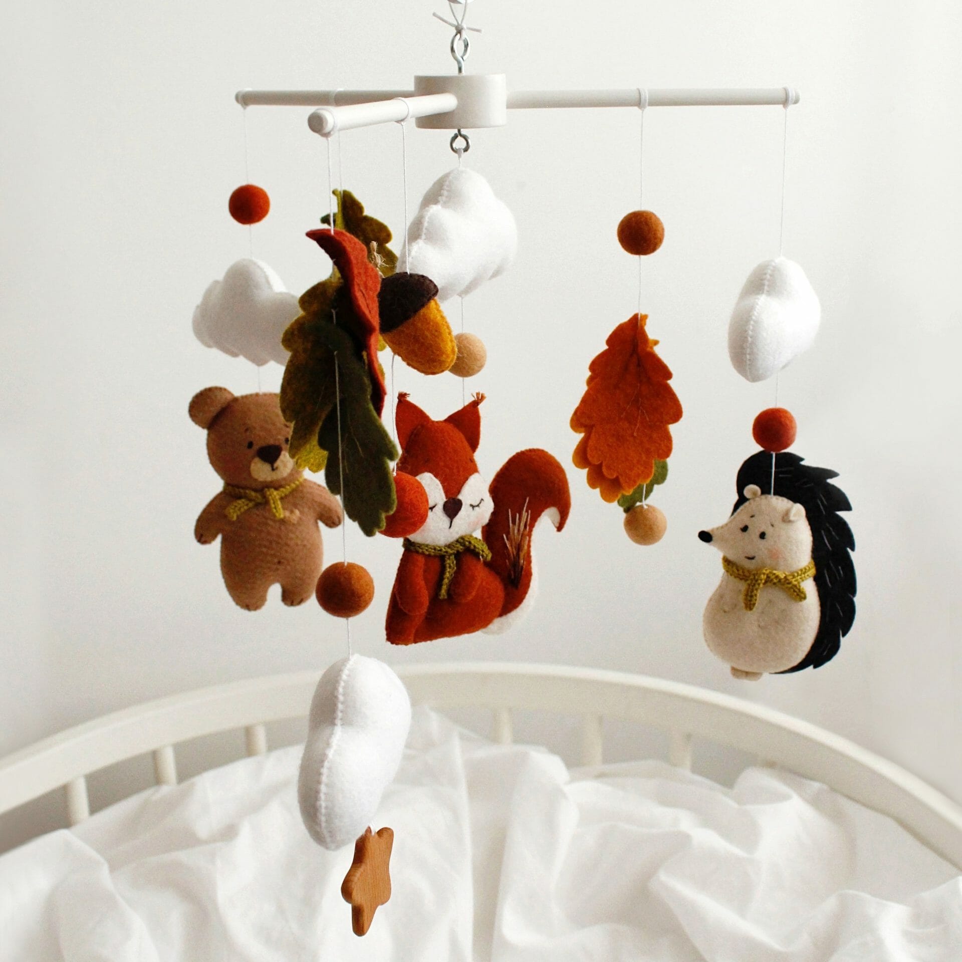 Hanging over the baby cot autumn forest woodland nursery crib mobile with cute squirrel, bear, hedgehog, many leaves and clouds.