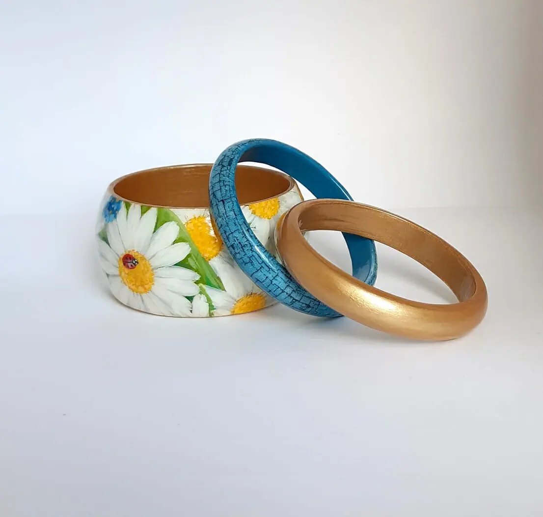 A set of three bracelets . A bracelet with daisies , a blue bracelet and a golden bracelet . Beautiful Handmade jewelry.