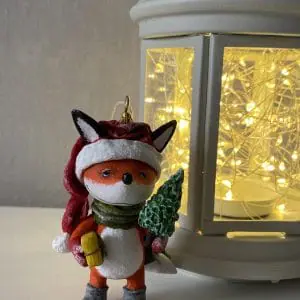 handmade christmas toy fox in a Santaclaus hat with a Christmas tree and a gift in his hand