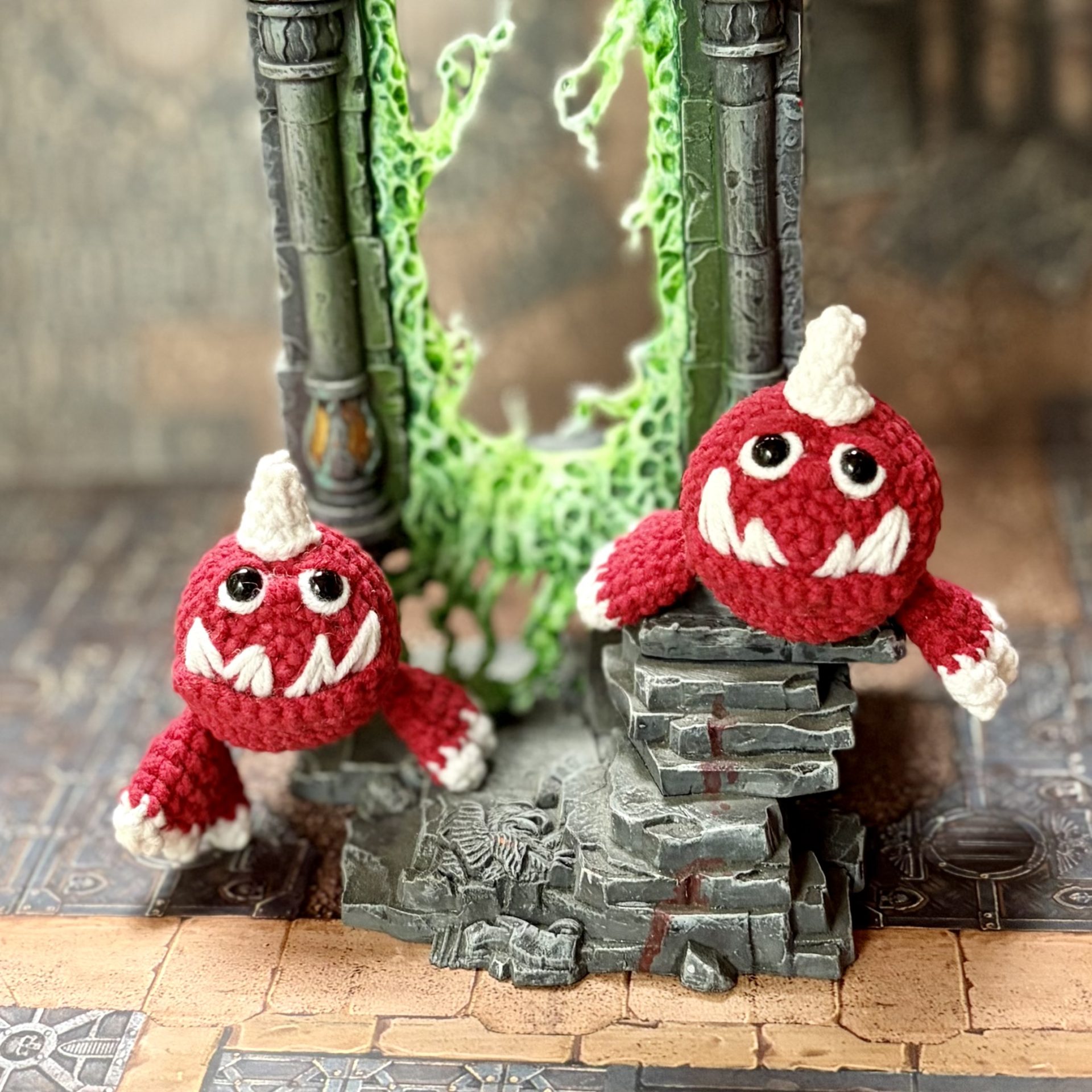 Pocket Squig Crochet Pattern. Warhammer Fantasy Amigurumi PDF 3 Crochet pattern showing two small red Squigs inspired by Warhammer in front of a glowing green portal