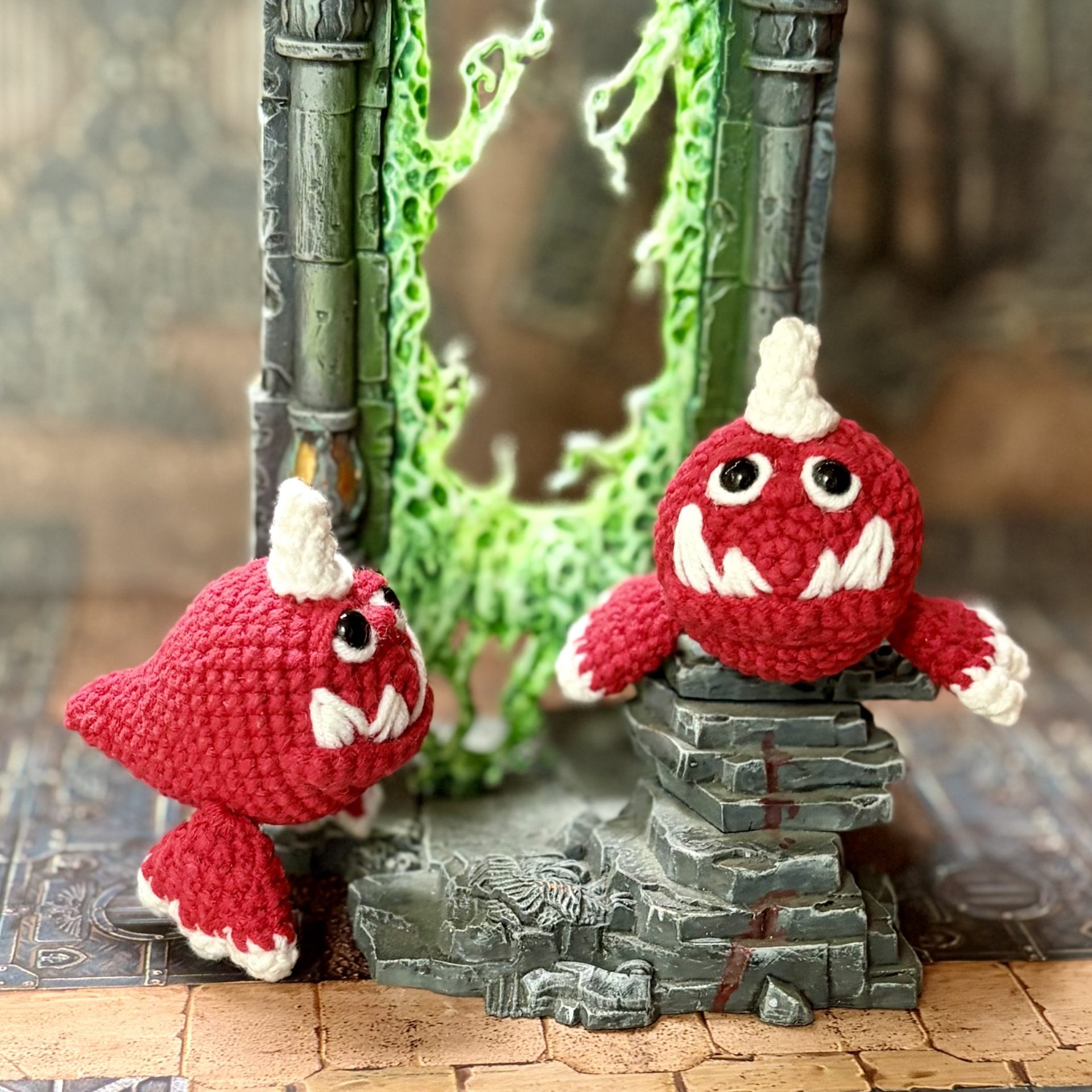 Pocket Squig Crochet Pattern. Warhammer Fantasy Amigurumi PDF 6 Two crochet Warhammer Squigs facing each other beside a glowing green warp portal in a fantasy dungeon
