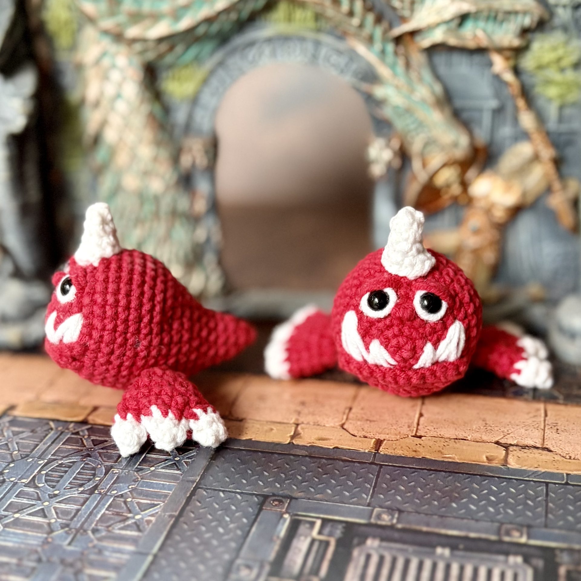 Pocket Squig Crochet Pattern. Warhammer Fantasy Amigurumi PDF 2 Two crochet Warhammer Squigs shown from the front and side on a fantasy dungeon floor with ancient stone ruins in the background
