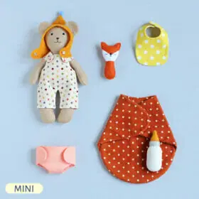 Handmade Mini Baby Bear stuffed animal in overalls and hat with baby set lying next to him: baby bottle, fox rattle, sleeping bag, bib and diaper