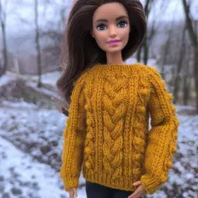 Barbie doll in mustard knit sweater with pinecone embellishments. Stylish winter fashion for a trendy doll look.
