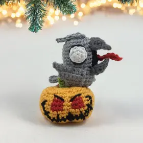 Plush crochet zombie bird on evil pumpkin amigurumi toy, spooky Halloween handmade pattern.
