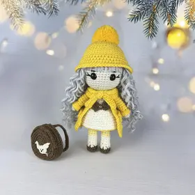 Plush crochet doll in a yellow coat and beanie with a pompom, handmade amigurumi pattern.