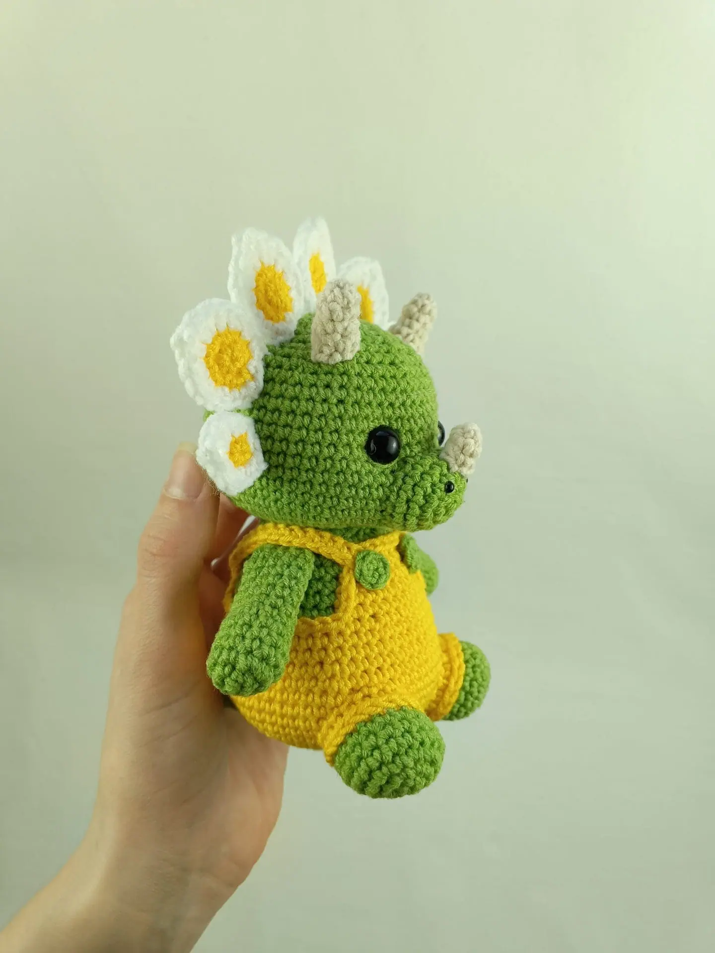 Flowers Dino Crochet Pattern Cute Triceratops Amigurumi Toy 2 Crochet plush amigurumi triceratops dinosaur with daisy flower petals and yellow overalls, digital crochet pattern.