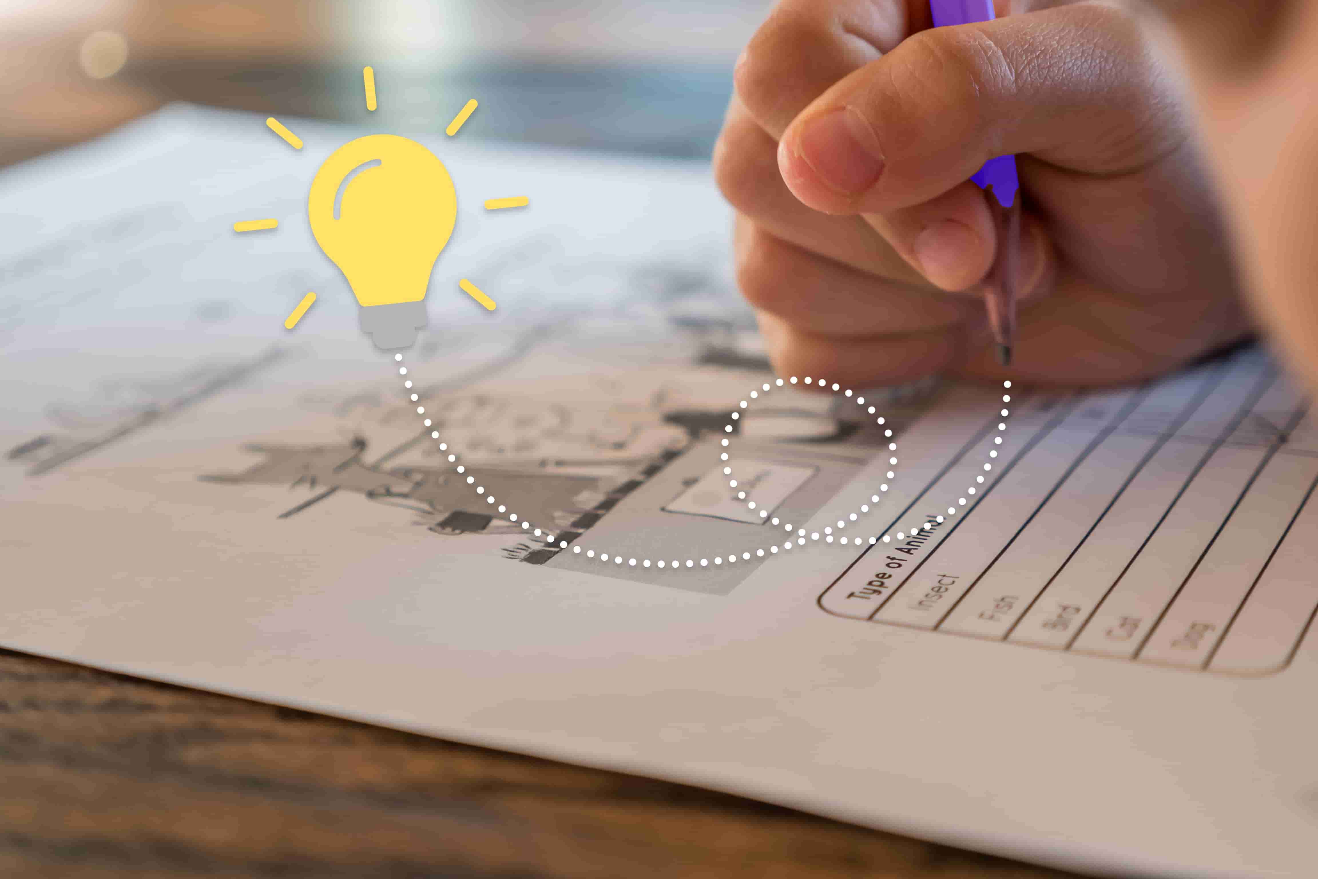 Una mano che tiene una penna scrive su un foglio di carta. Una vignetta raffigurante una lampadina compare a sinistra della mano.