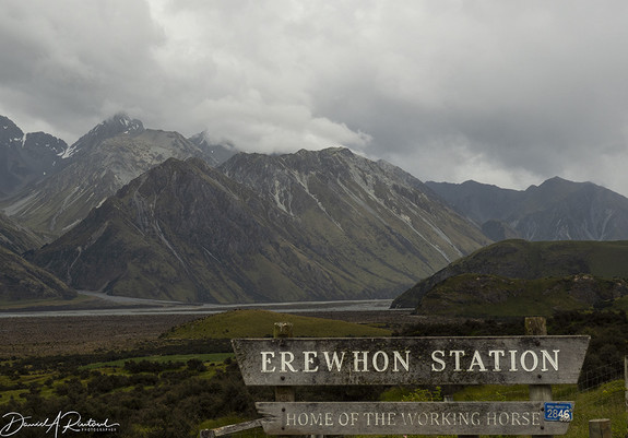 high mountain peaks, gathering clouds, distant river, and a sign that reads "Erewhon Station"