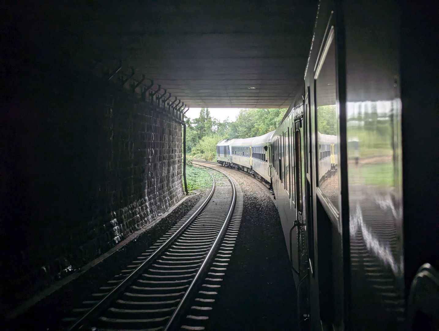 A photo of a train going through a tunnel, with the front end of it being perfectly visible from there as the train goes into a left curve.